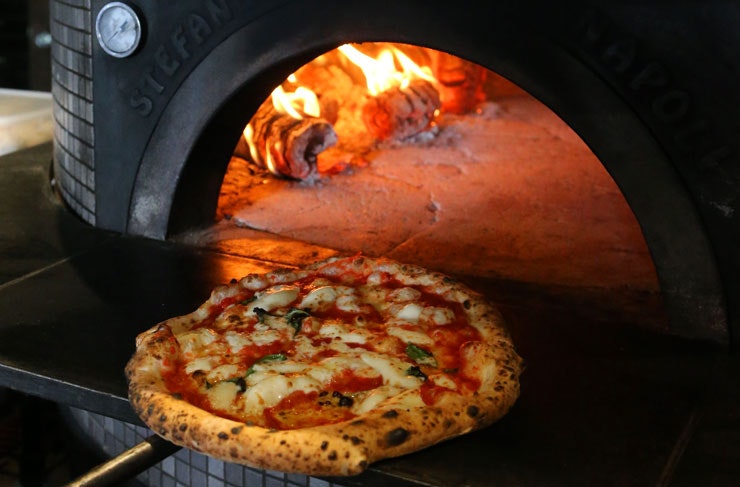 A Napoli-style Margherita pizza being retrieved from a stone pizza oven.